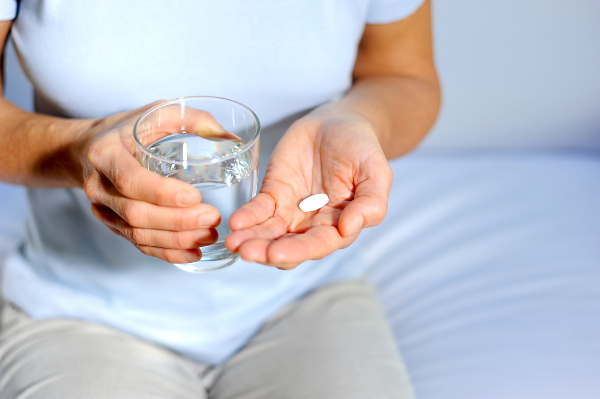 Rinforzare ossa e articolazioni: donna tiene in mano un bicchiere d'acqua e una pastiglia 