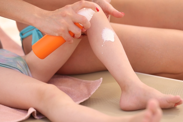 Concept per pelle dei bambini in estate: genitore applica crema solare sulla gamba di un bambino