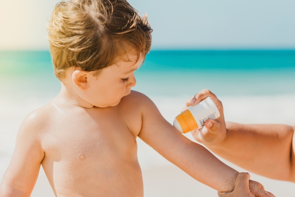 Concept per pelle dei bambini in estate: genitore applica crema solare sul braccio di un bambino