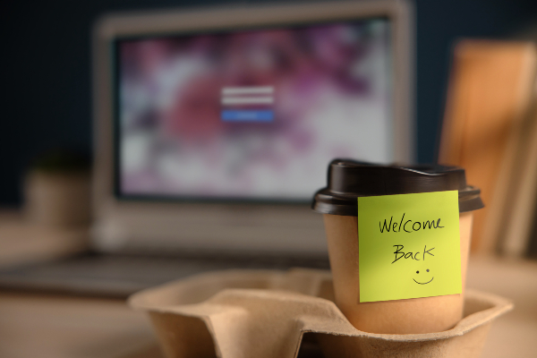 Concept per sindrome da rientro: tazza da caffè con scritta ''welcome back'' posizionata su di una scrivania in ufficio