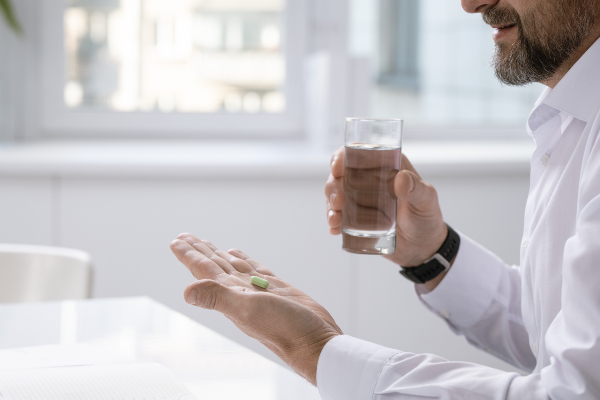 Concept per integrazione di Vitamine del Gruppo B: close up su mani di uomo che tengono una capsula di integratore e un bicchiere d'acqua
