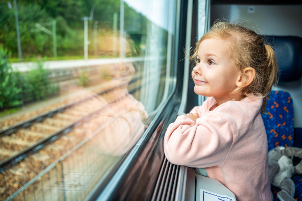 Concept per bambini in viaggio: bambina sorridente guarda fuori dal finestrino di un treno.