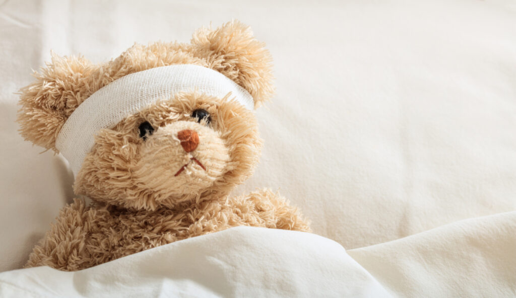Concept per mal di testa bambini: un peluche a letto, con la testa fasciata da una benda
