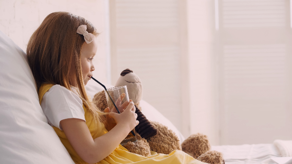 Concept per acetone nei bambini: bambina beve con una cannuccia dell'acqua seduta sul divano