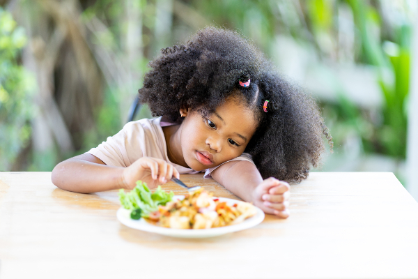 Concept per acetone nei bambini: bambina davanti a un piatto con atteggiamento inappetente