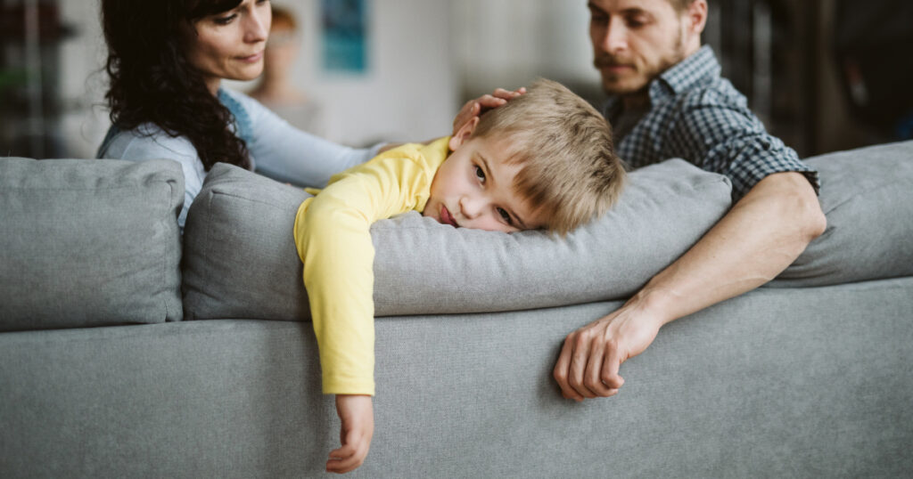Concept per acetone nei bambini:bambino con aria stanca sul divano tra mamma e papà