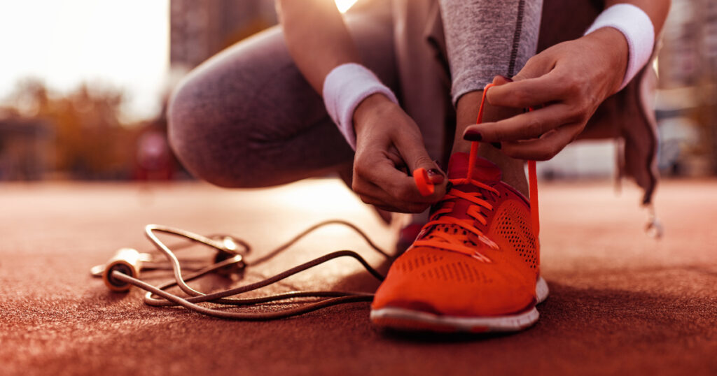 Concept per ripresa dell'attività fisica dopo le vacanze: close up su donna che si allaccia le scarpe da jogging