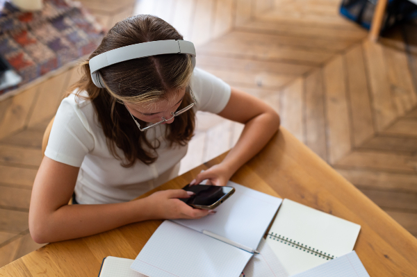 Concept per occhi stanchi: ragazza vista dall'alto con occhiali, intenta a guardare lo smartphone